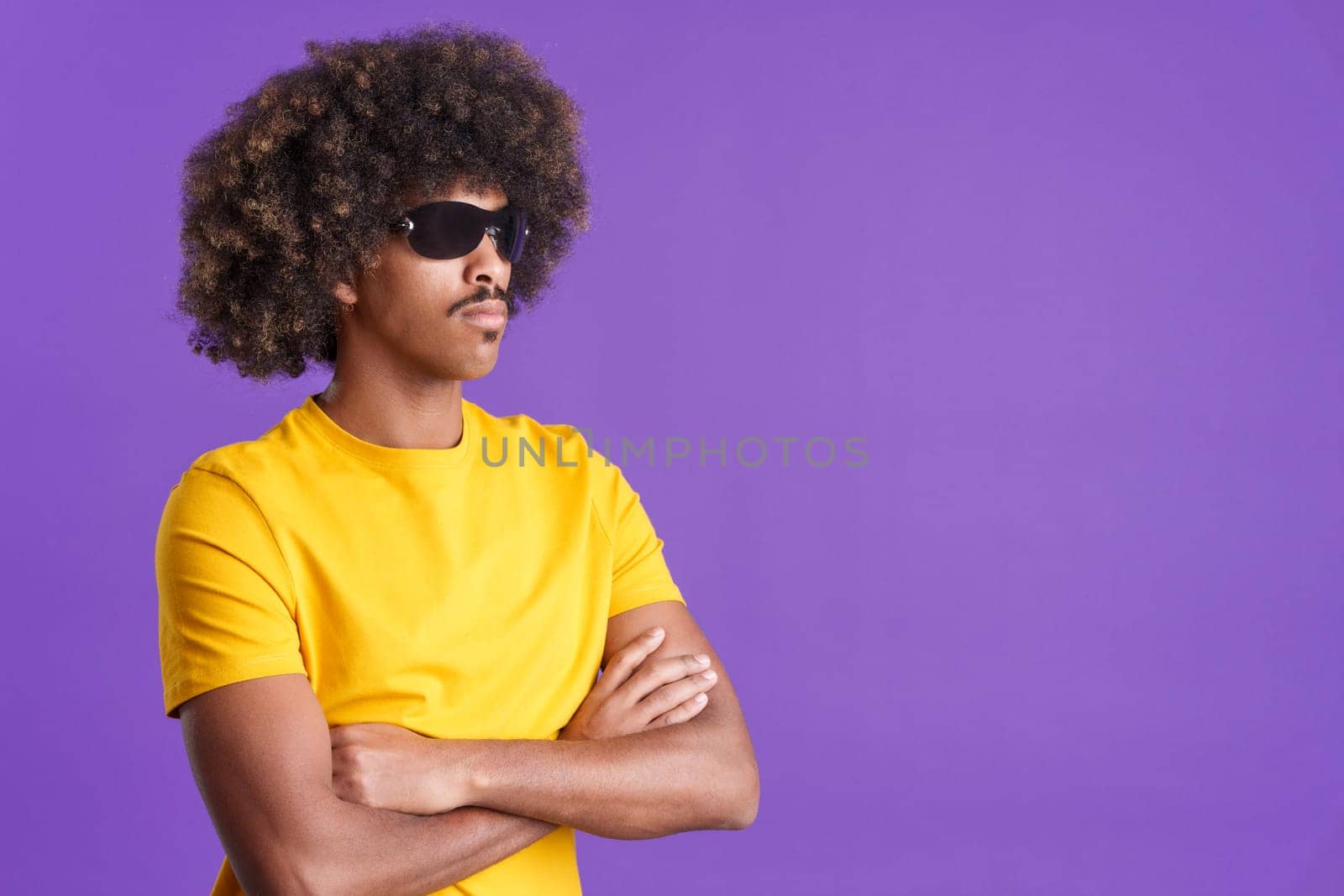 Serious african man with curly hair wearing sunglasses posing with arms crossed in studio