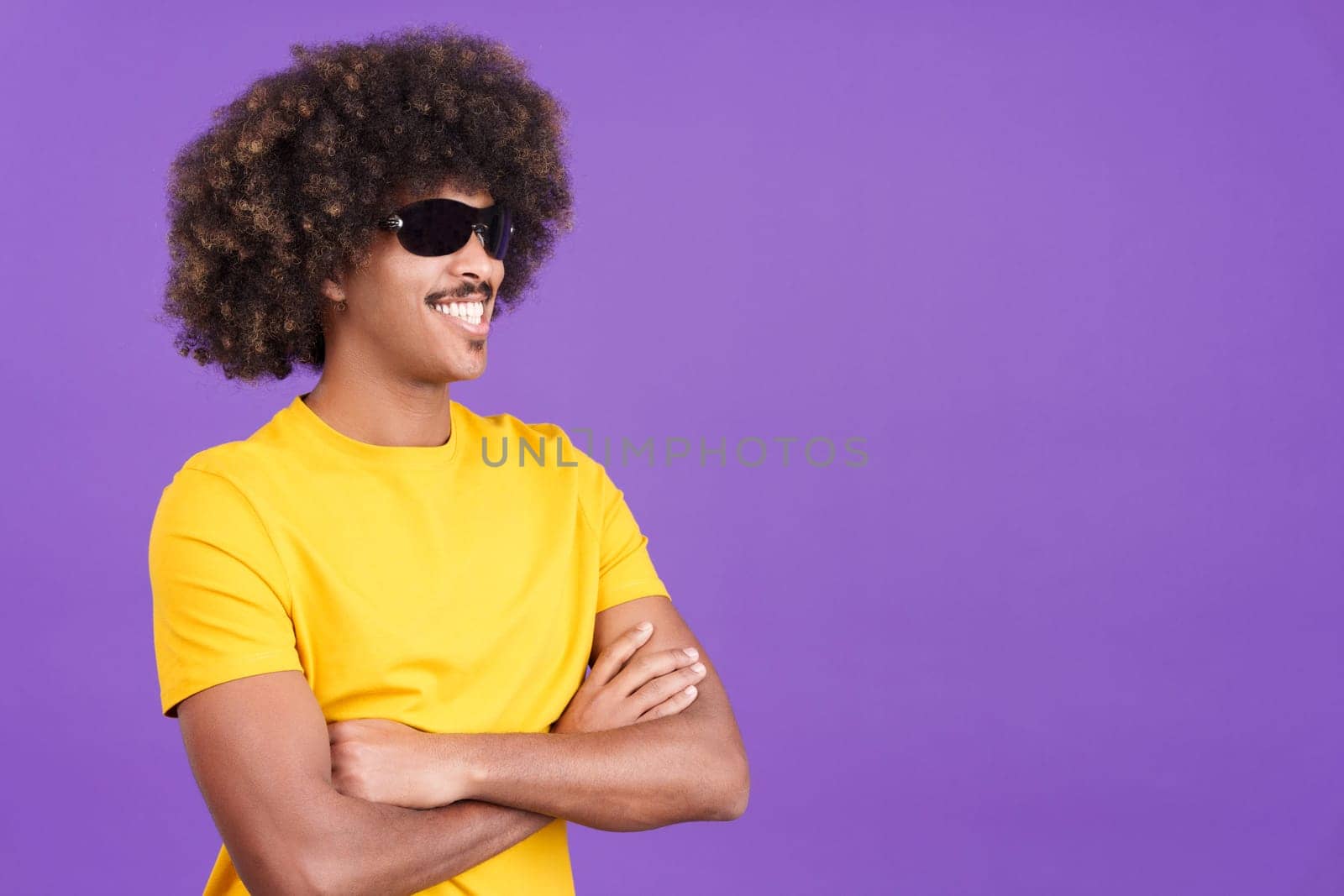 Smiley african man with curly hair wearing sunglasses posing with arms crossed in studio
