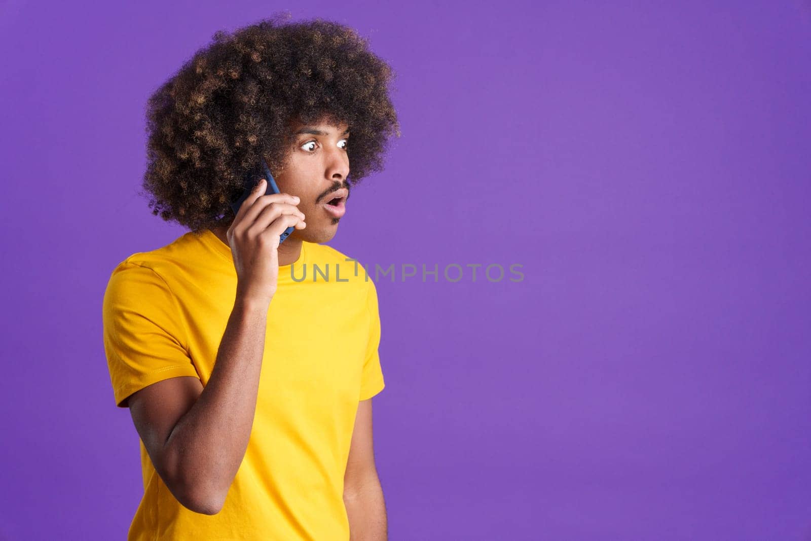 Stylish surprised african man with curly hair talking to the mobile in studio