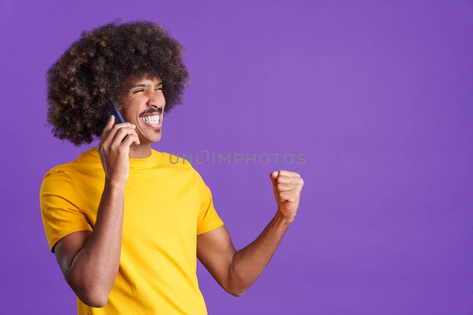 African man celebrating raising the fist while taking to the mobile in studio