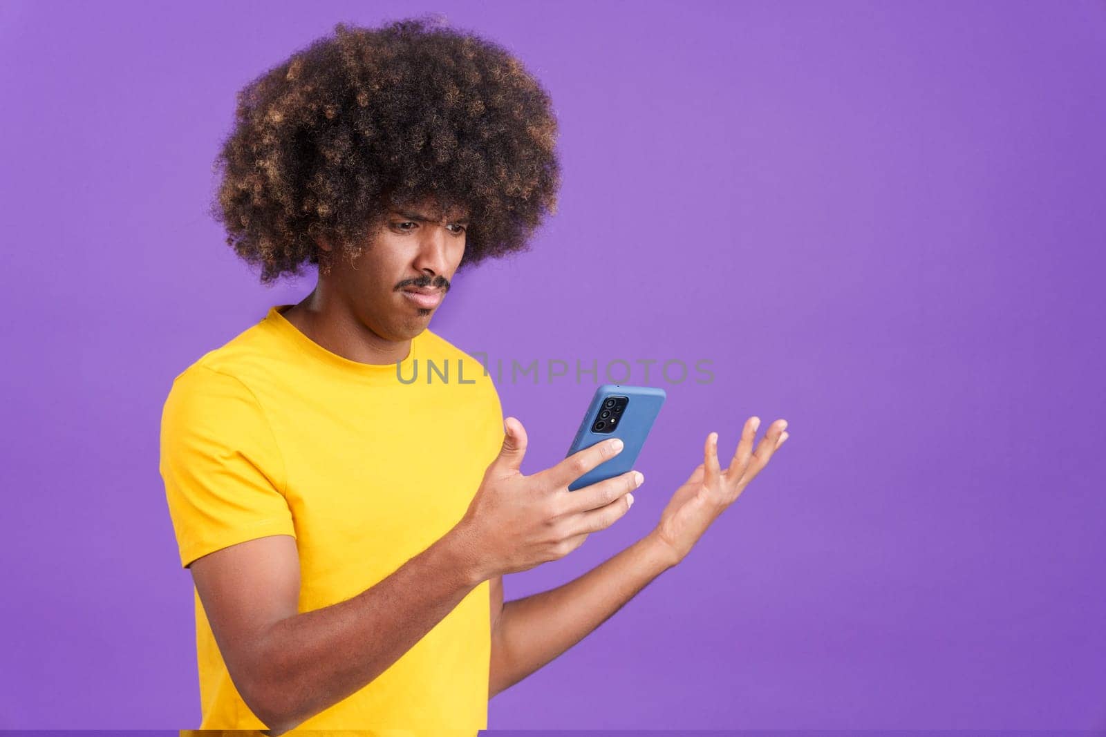 African man with curly hair gesturing worried while using a mobile in studio
