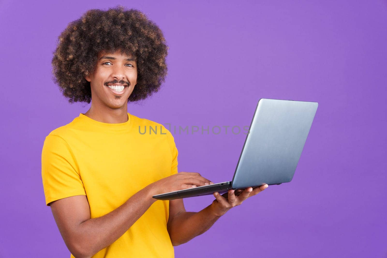 Smiley african man looking at the camera standing and using a laptop in studio