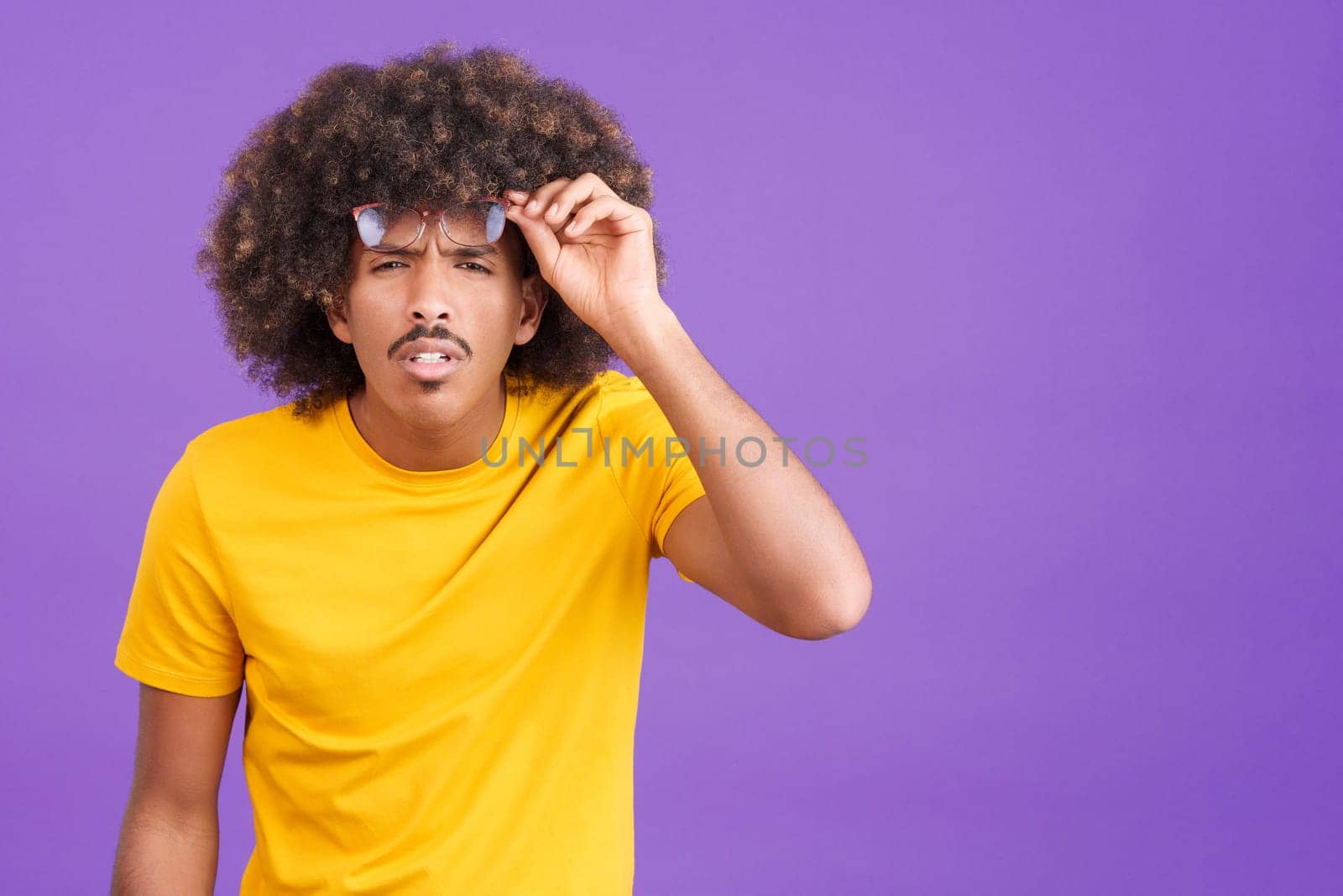 African man with curly hair taking off her glasses to see far away in studio