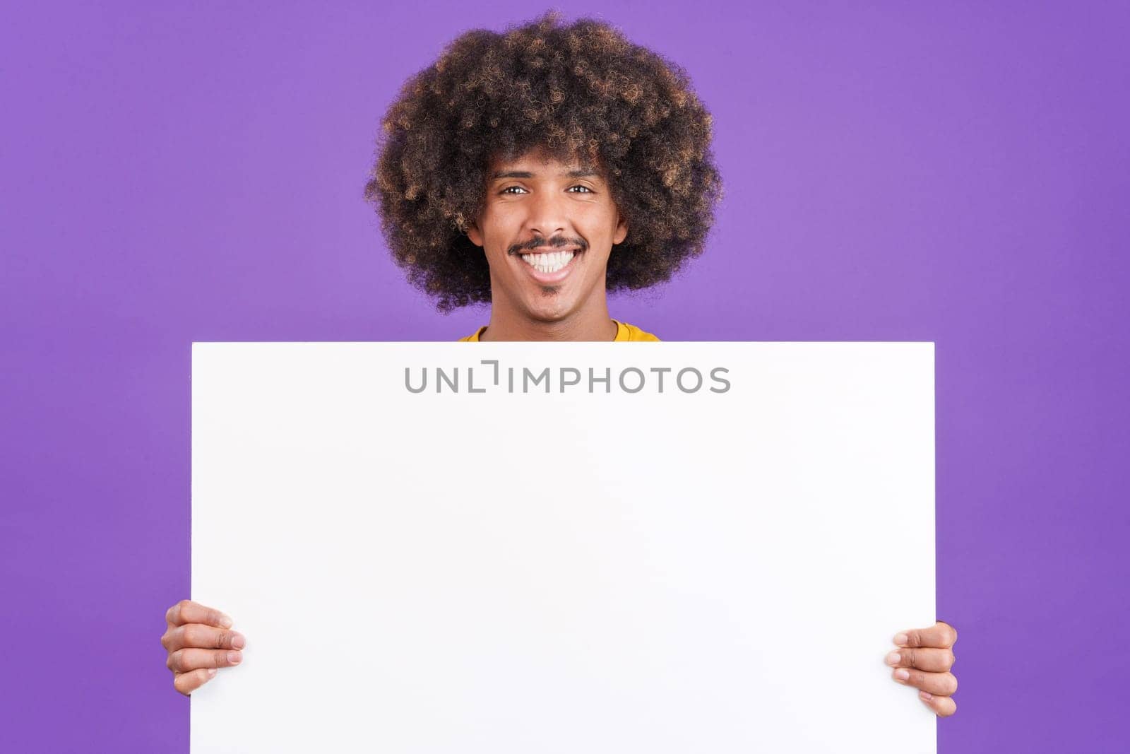 Smiley african man with curly hair holding a blank panel in studio