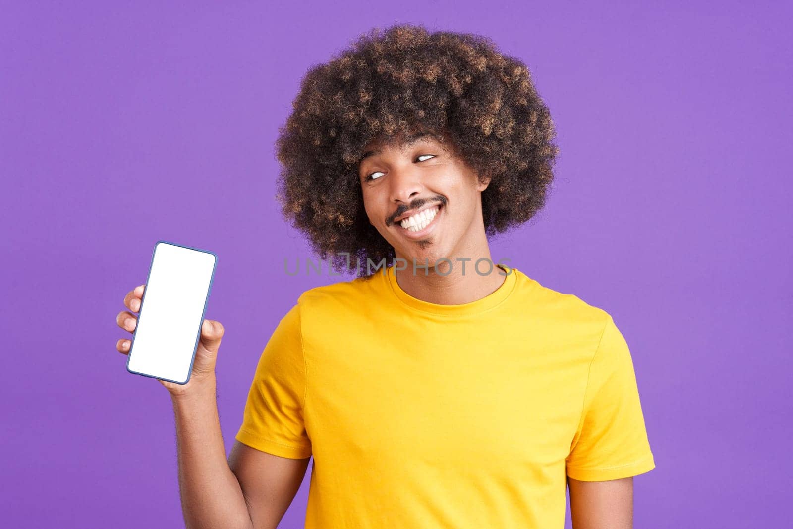 Smiley african man holding a mobile with a blank screen. Purple background