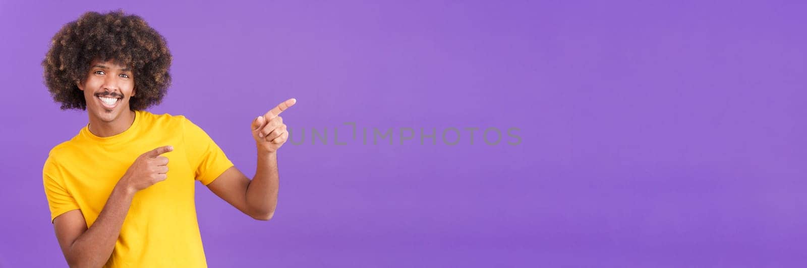 Cool and smiley african man gesturing to indicate a blank space to the side in studio