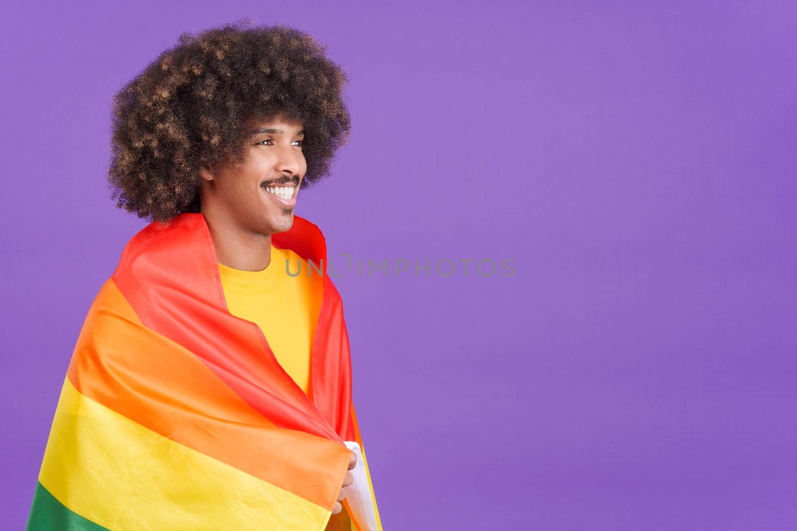 Smiling african man smiling at camera wrapped with a lgbt flag in studio
