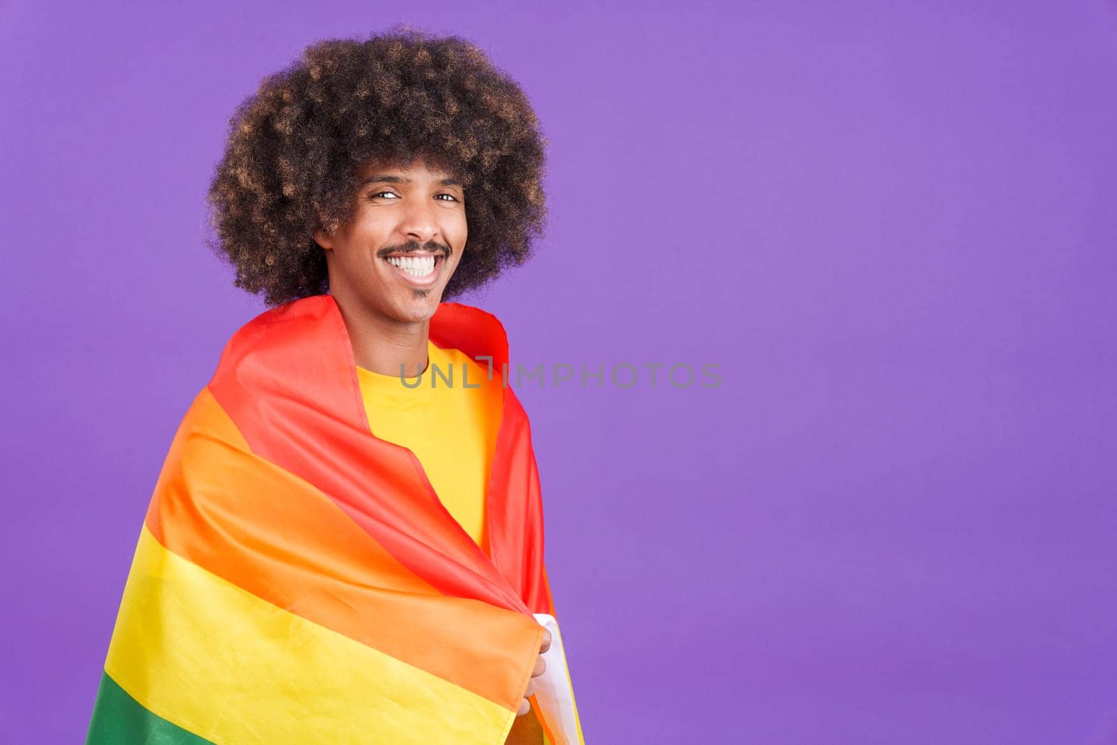 Happy african man smiling at camera wrapped with a lgbt flag in studio