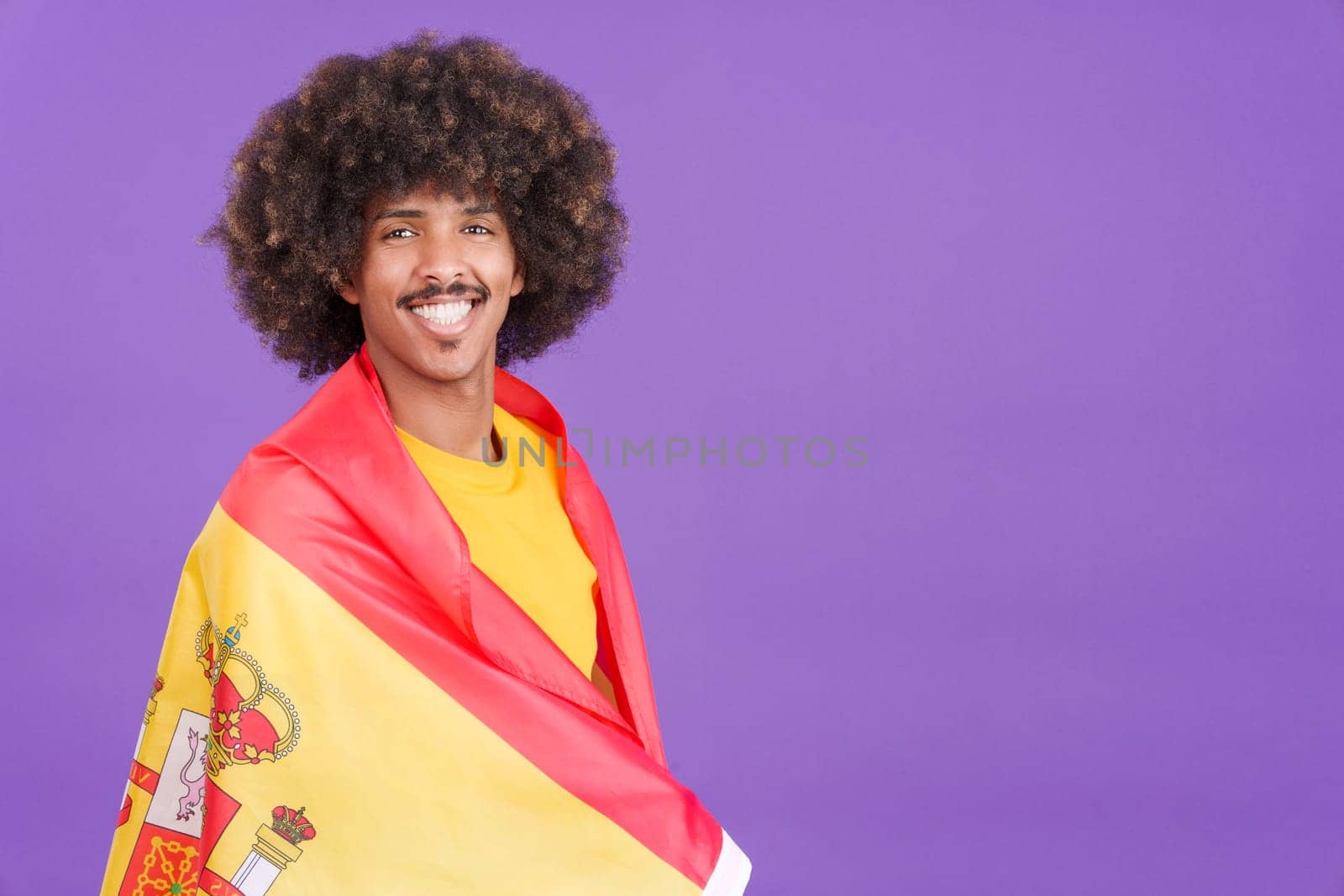 African man smiling at the camera wrapping with a spanish flag in studio