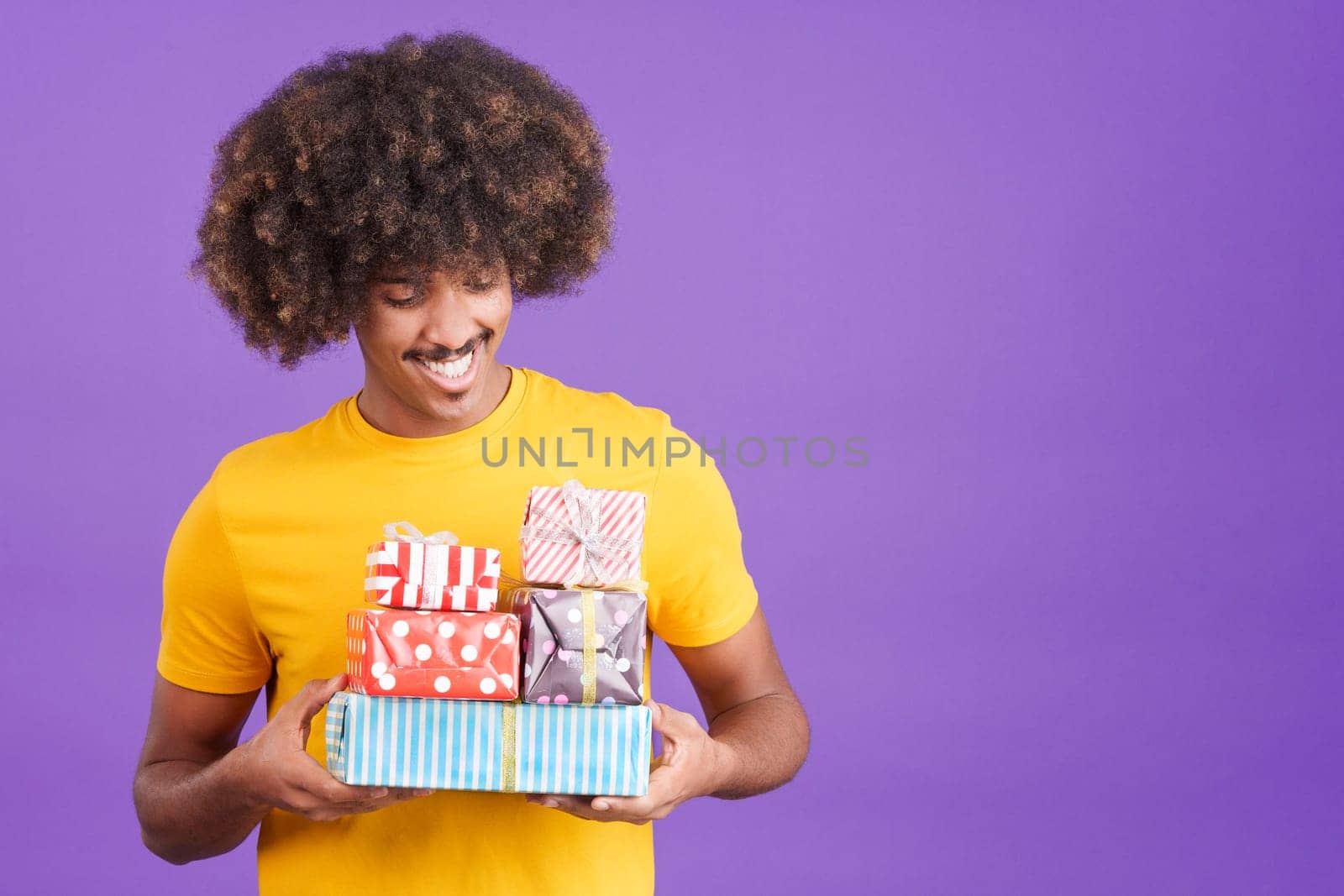Stylish african man with curly hair smiling with many gifts in the hands in studio