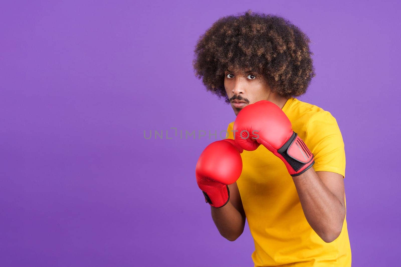 African man with boxing gloves in fight pose looking at the camera in studio