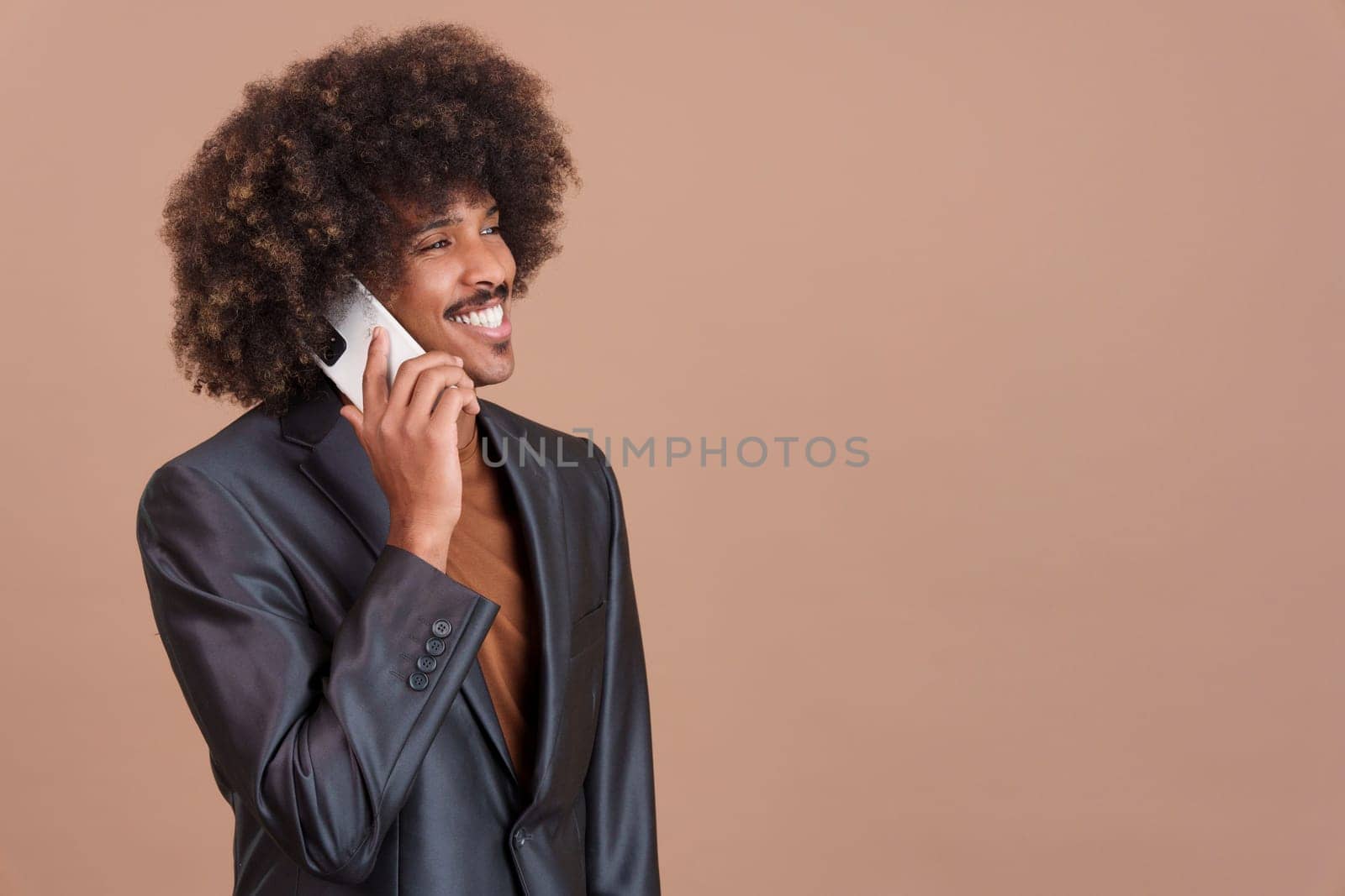 African elegant man with curly hair and black jacket talking to the mobile phone in studio