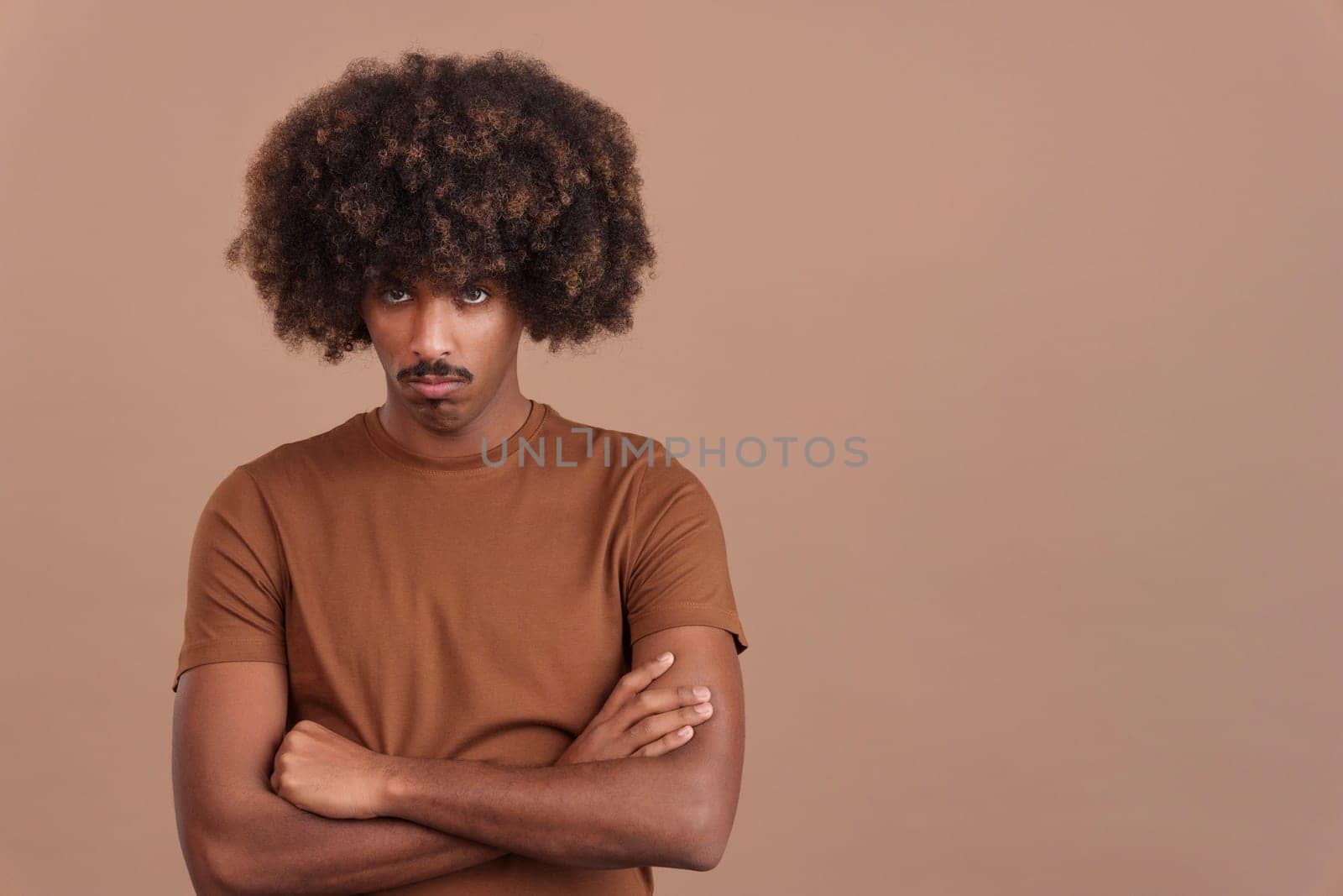 African man with afro hair crossing the arms while looking at camera with an angry expression in studio