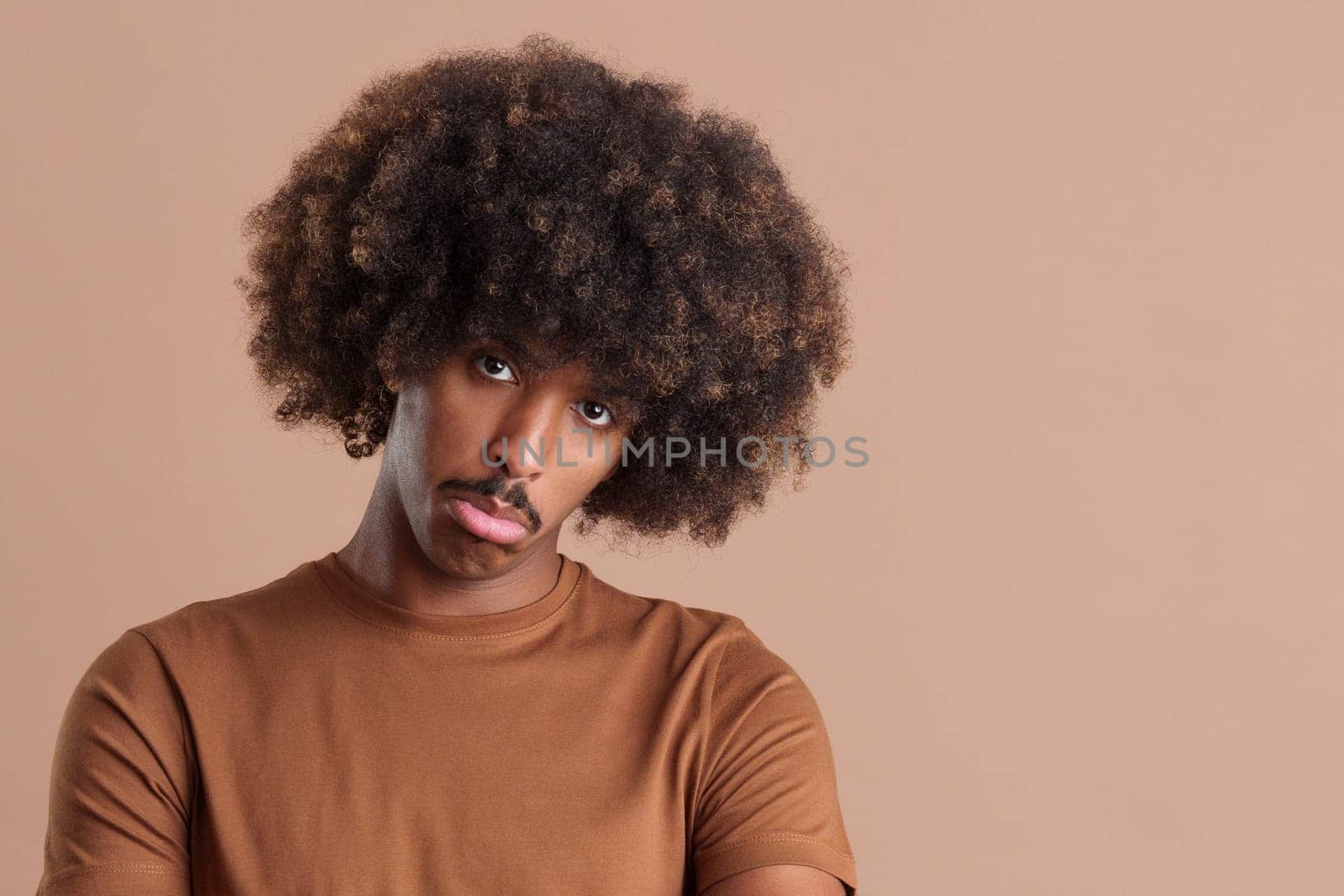 African man with curly hair looking at the camera with sad expression in studio