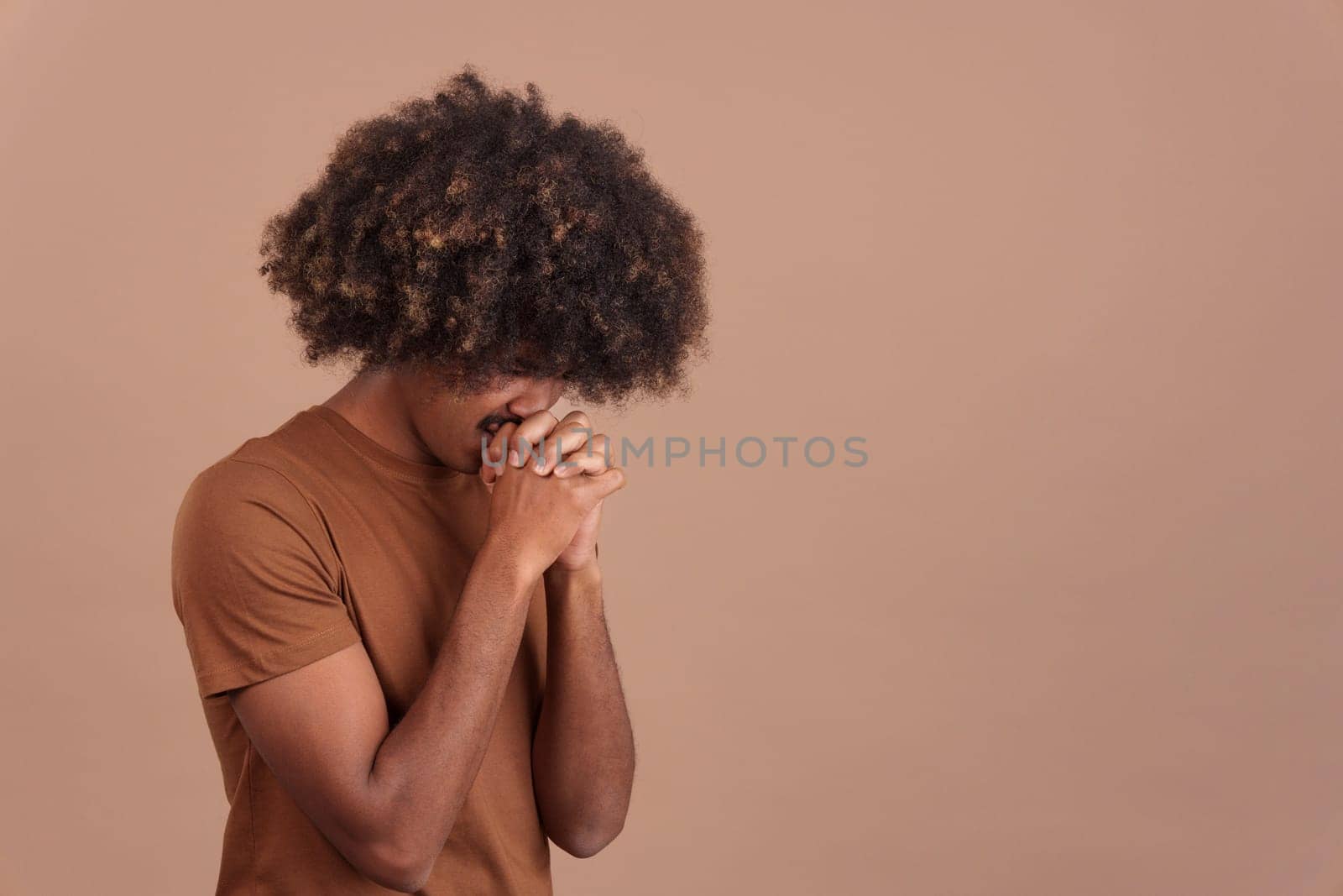 African man with curly hair praying with folded hands and closed eyes in studio