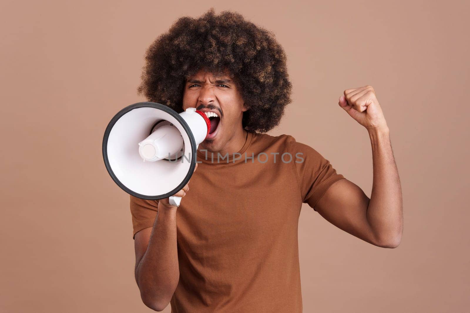 Upset african man with curly hair shouting using a loudspeaker in studio