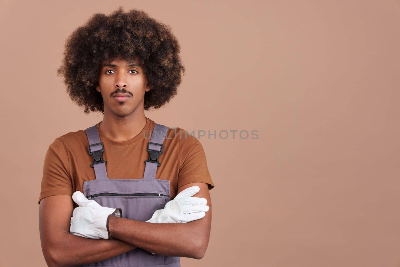 Serious african man carpentry worker looking at camera with the arms crossed in work uniformin studio