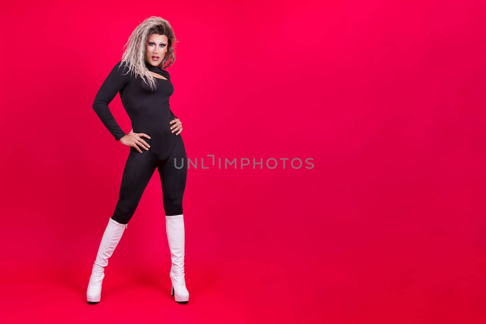 Stylish transgender person posing while looking at the camera in studio with red background