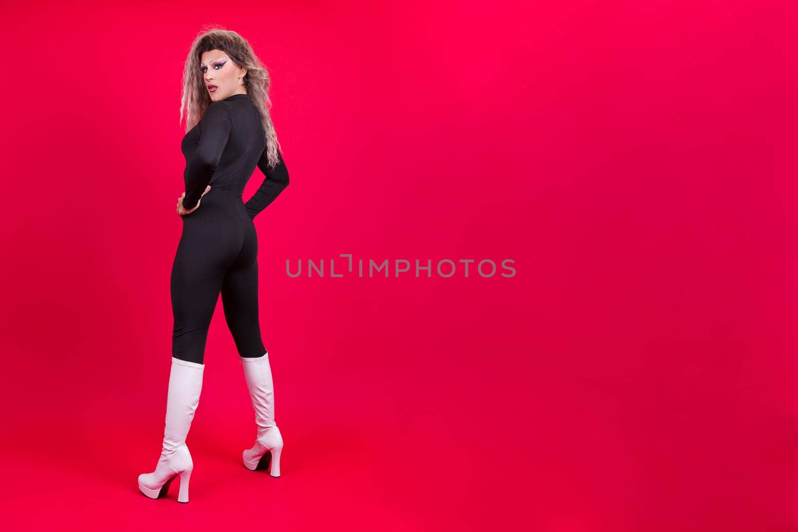Sensual drag queen person turning to look at the camera in studio with red background