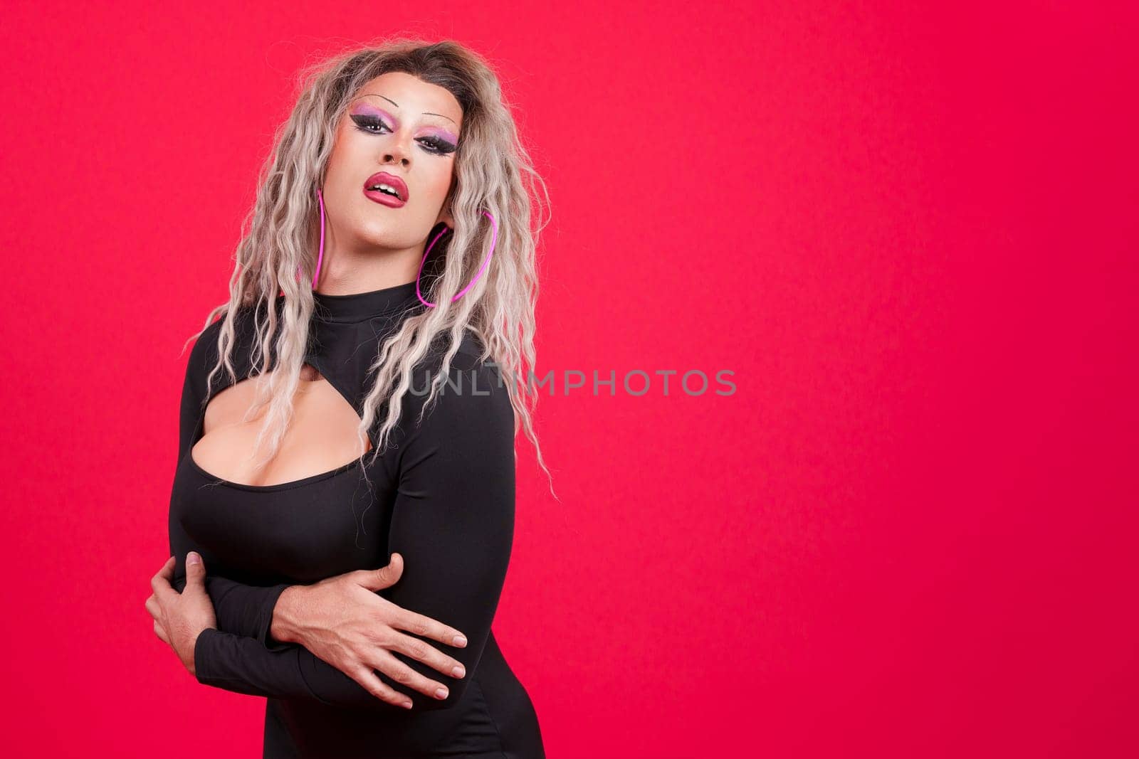 Sexy transgender person with make up looking at the camera in studio with red background