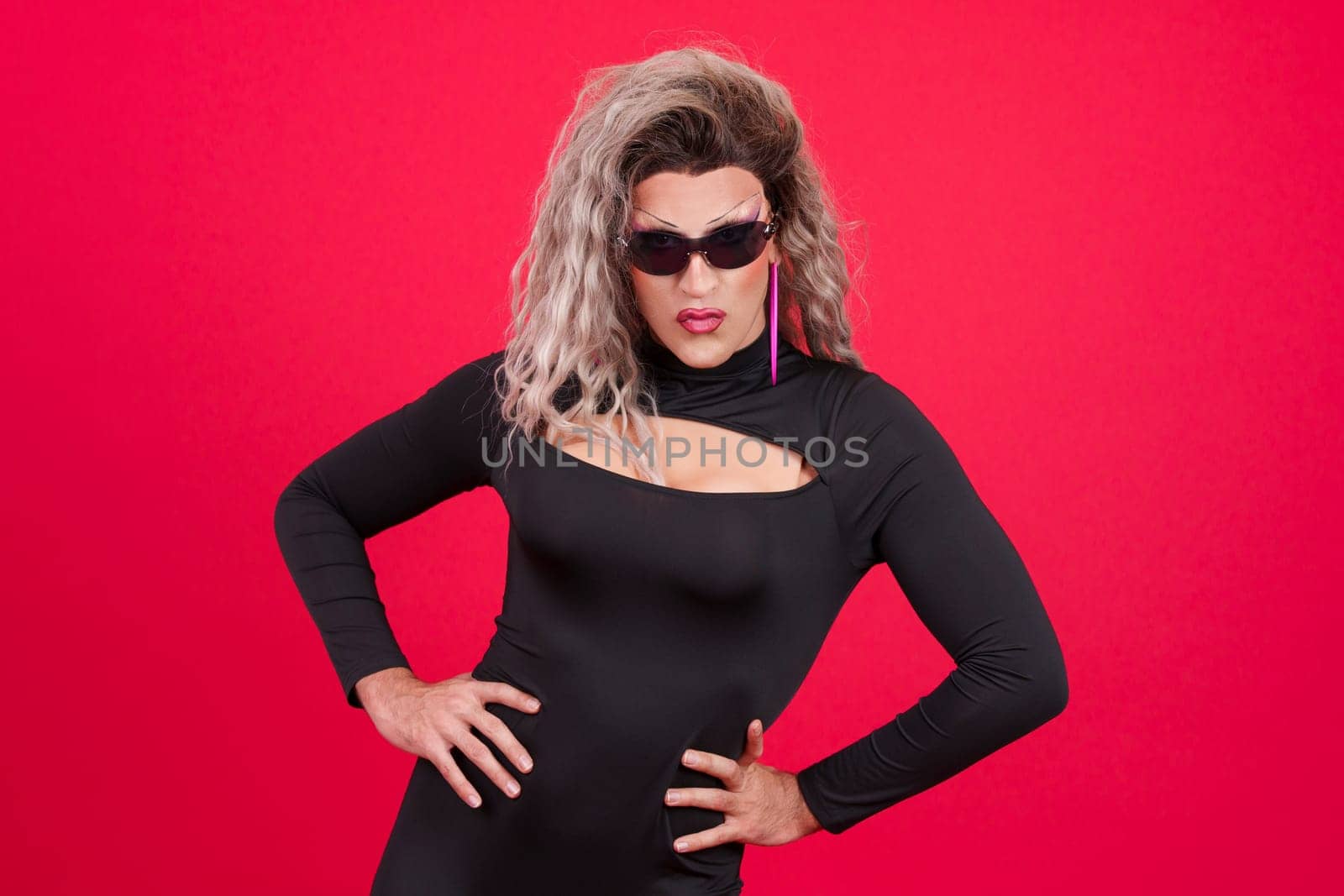 Drag queen person wearing sunglasses posing with rebel attitude in studio with red background