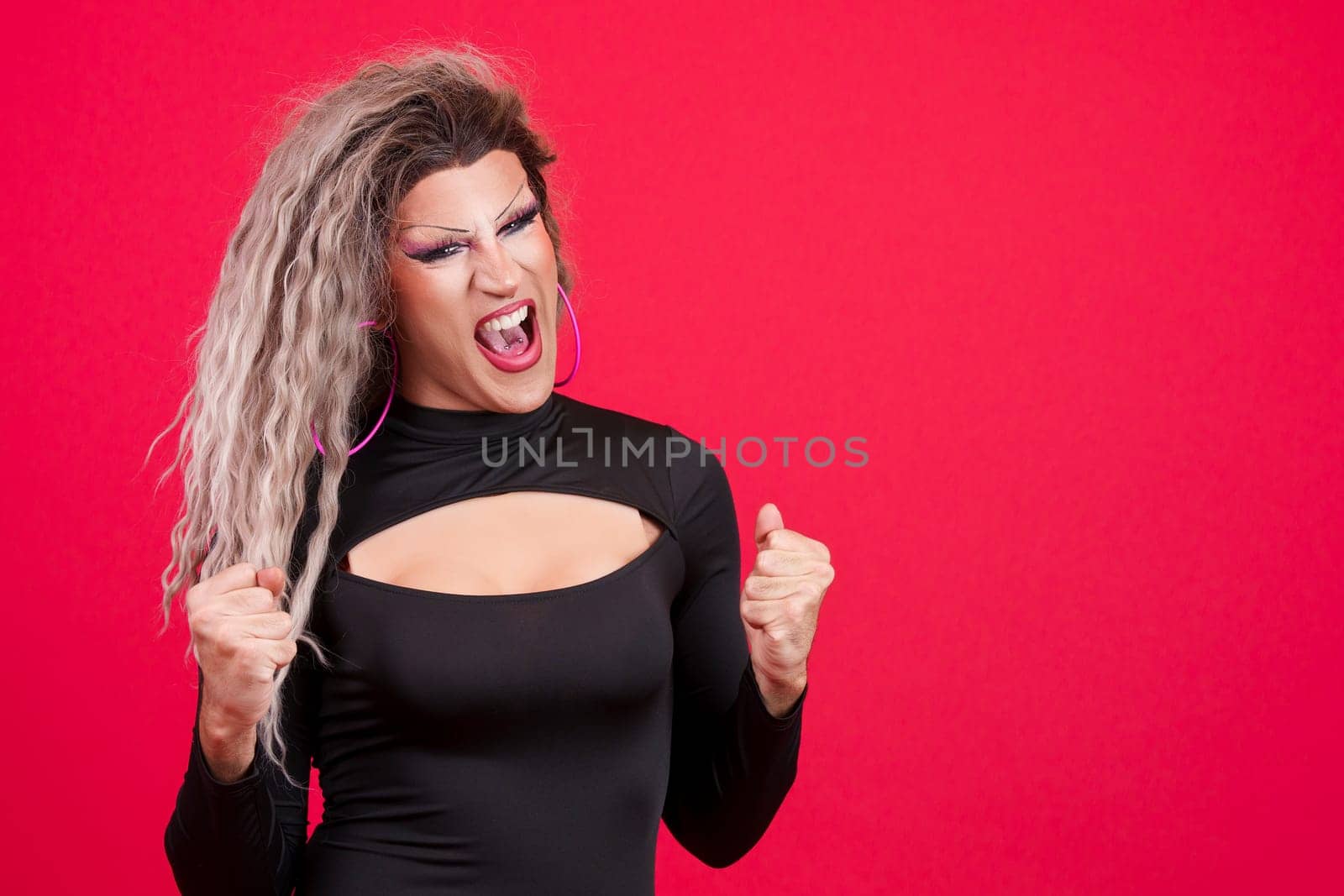 Passionate transgender person with make up celebrating raising the fist in studio with red background