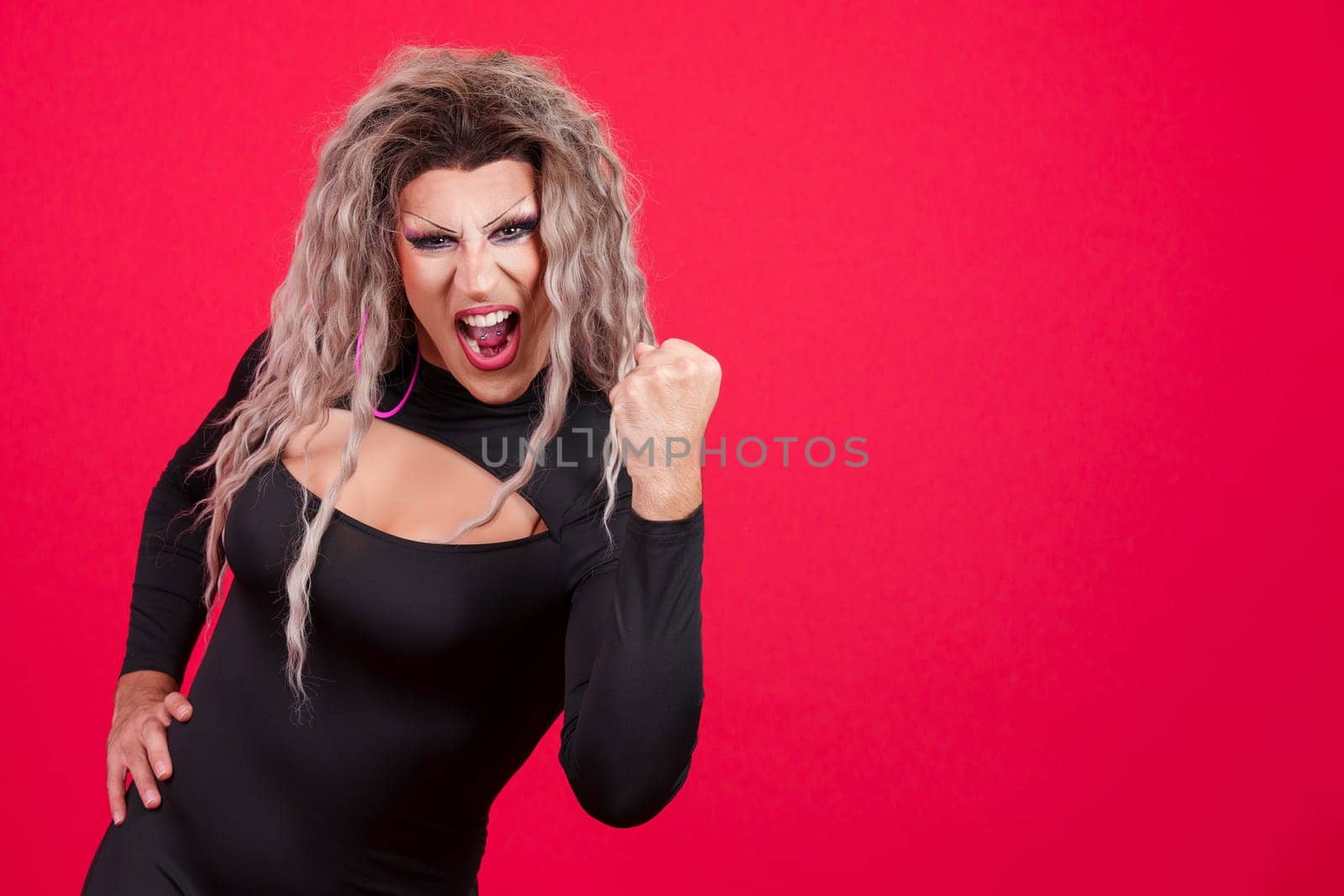 Emotional transgender person with make up celebrating raising the fist in studio with red background