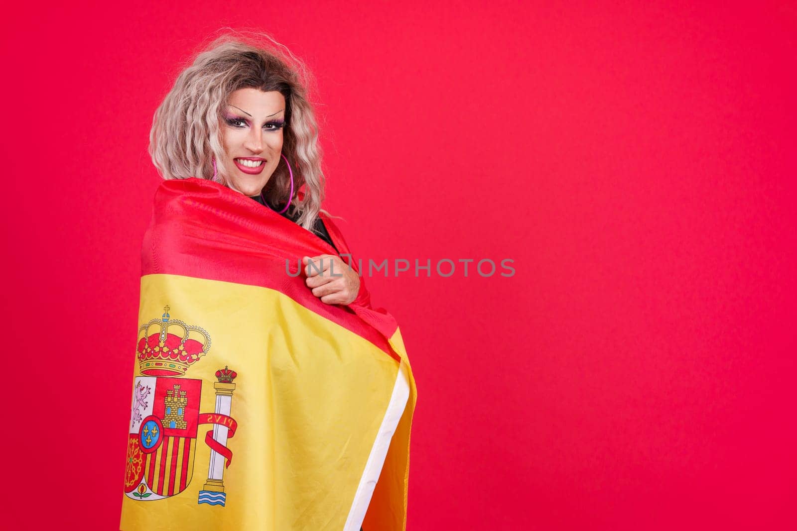 Smiley transgender person dressed as drag queen wrapping with a spanish flag in studio with red background