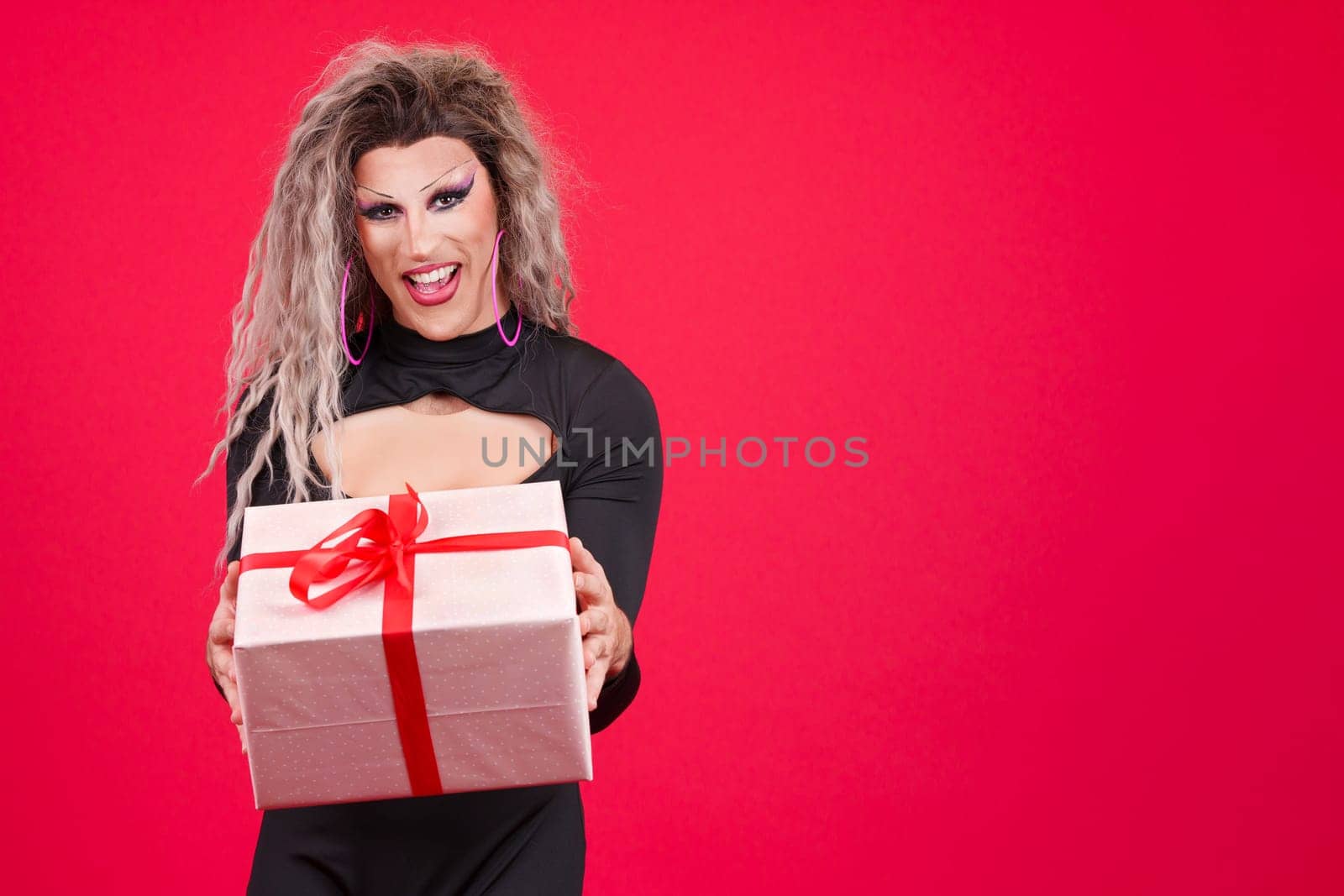 Happy transgender person dressed as drag queen smiling at camera while giving a gift