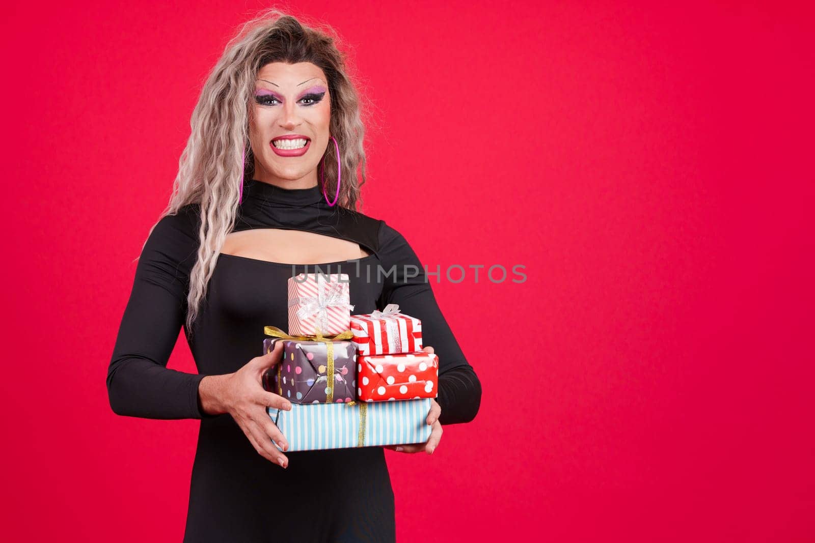 Smiley transgender person with make up holding many gifts in studio with red background