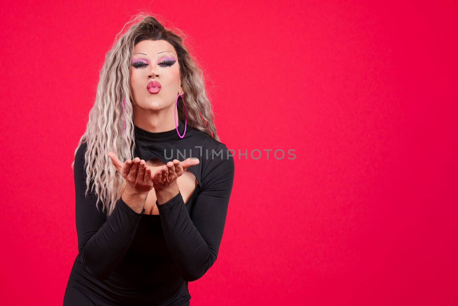 Transgender person dressed as drag queen blowing a kiss looking at camera in studio with red background