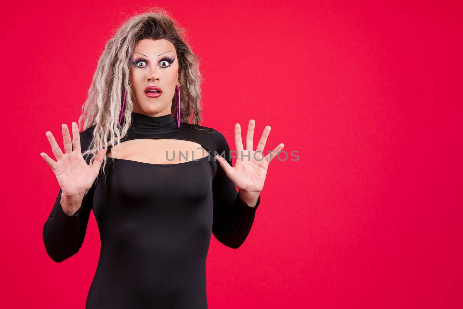 Surprised transgender person gesturing with the hands in fear in studio with red background