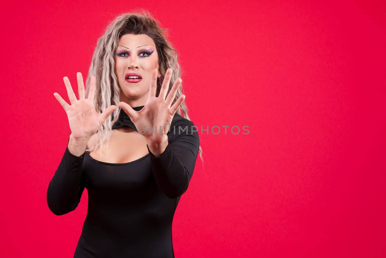 Transgender person gesturing with the hands in fear in studio with red background