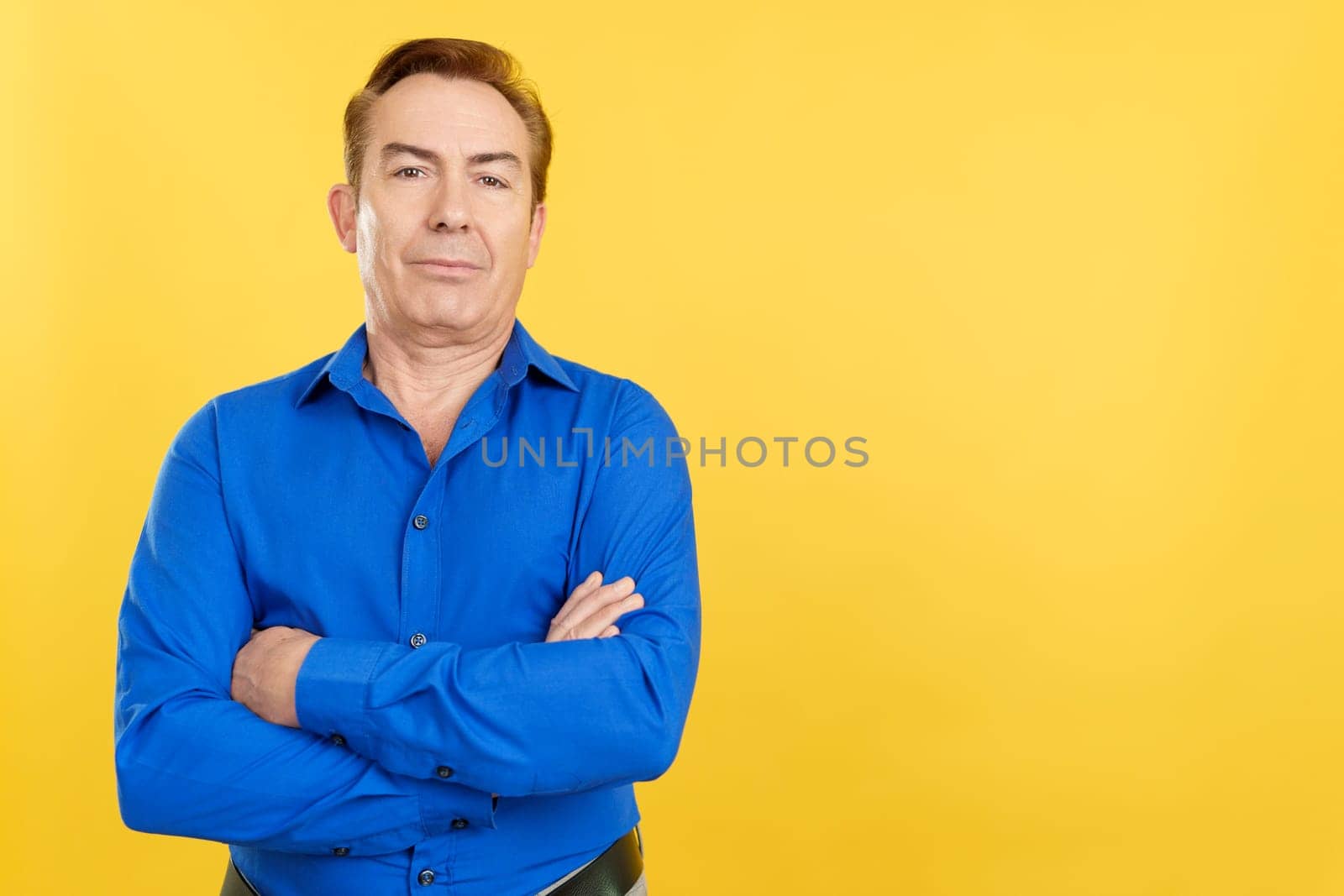Mature man standing and looking at the camera with arms crossed in studio with yellow background