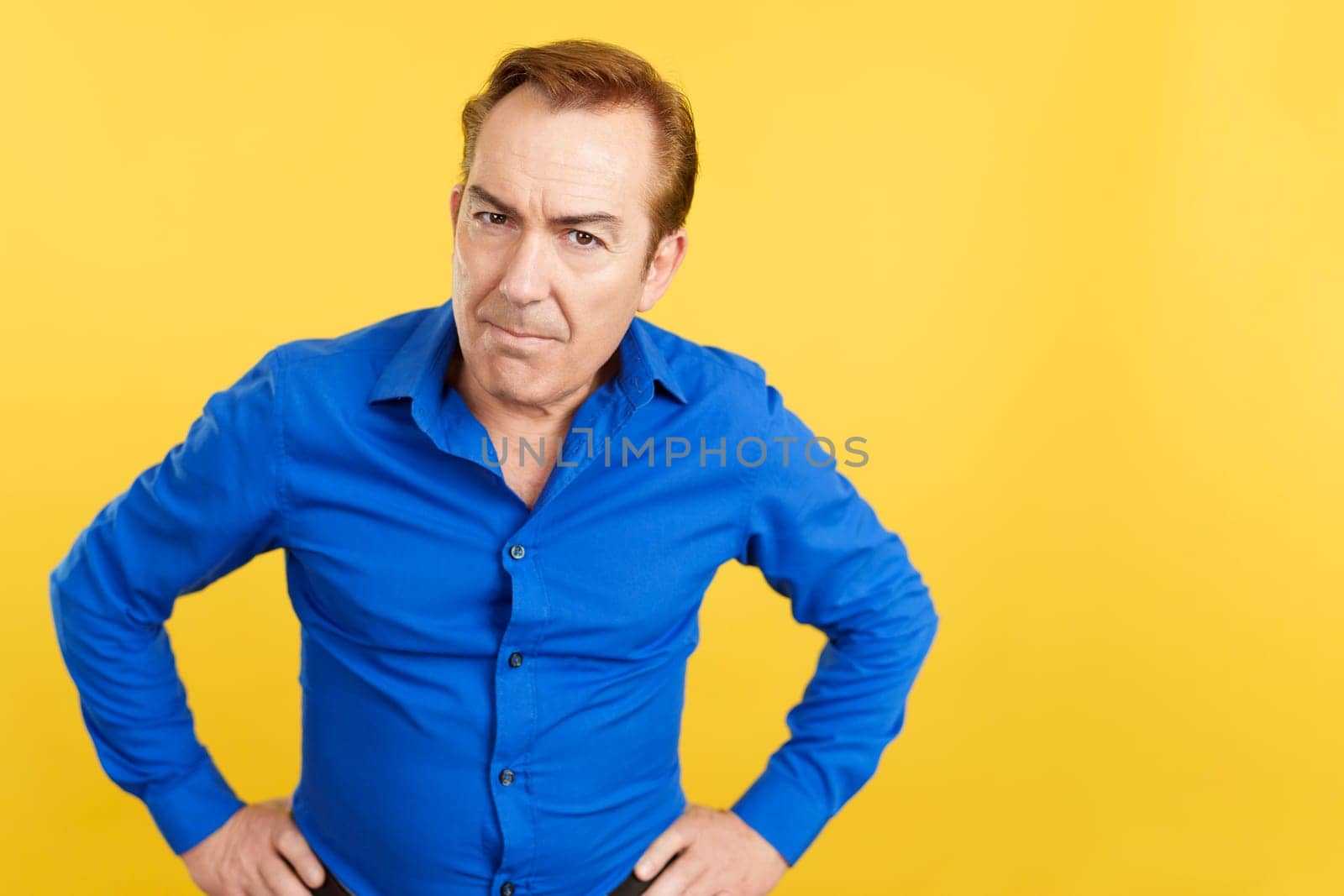 An angry mature man looking at the camera in studio with yellow background