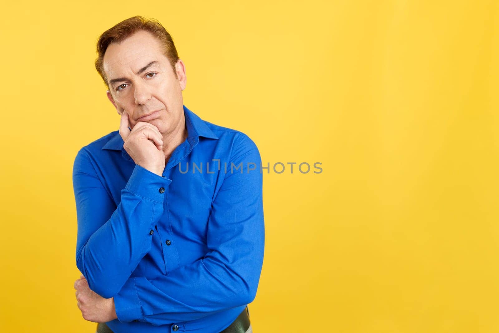 Mature man looking at camera and gesturing bored in studio with yellow background