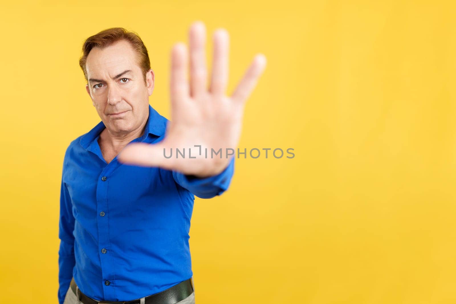 Mature man rejecting with the palm of the hand in studio with yellow background