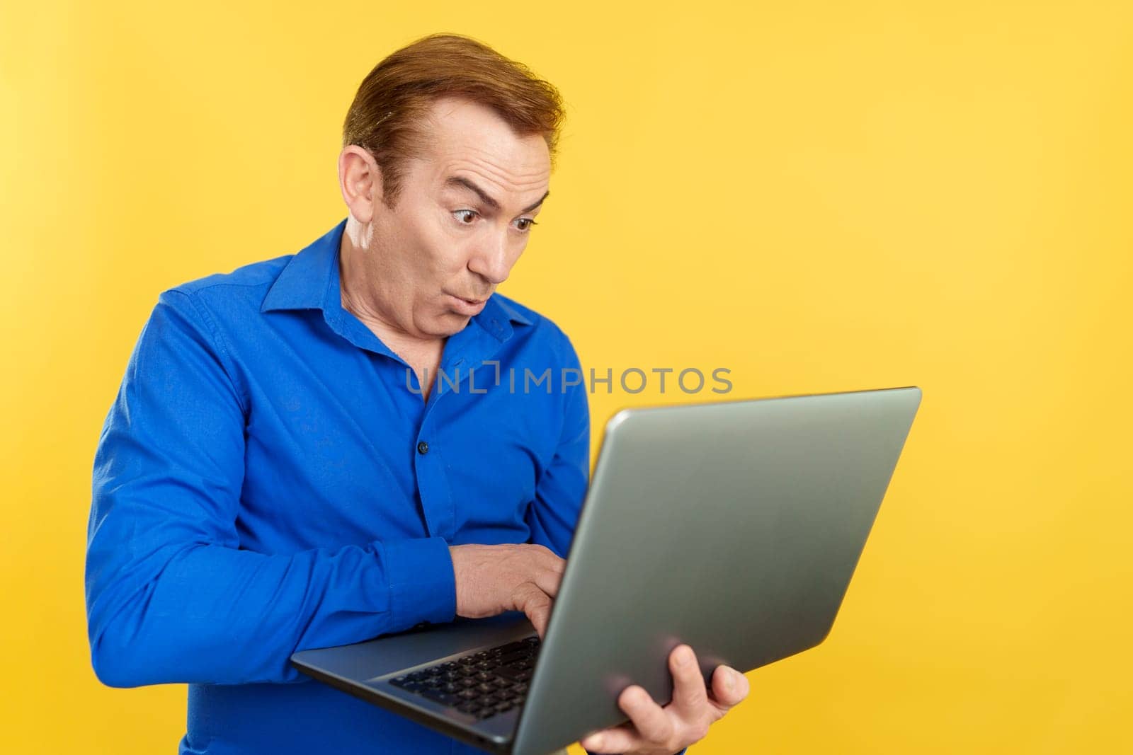 Mature man using a laptop with a surprised look in studio with yellow background
