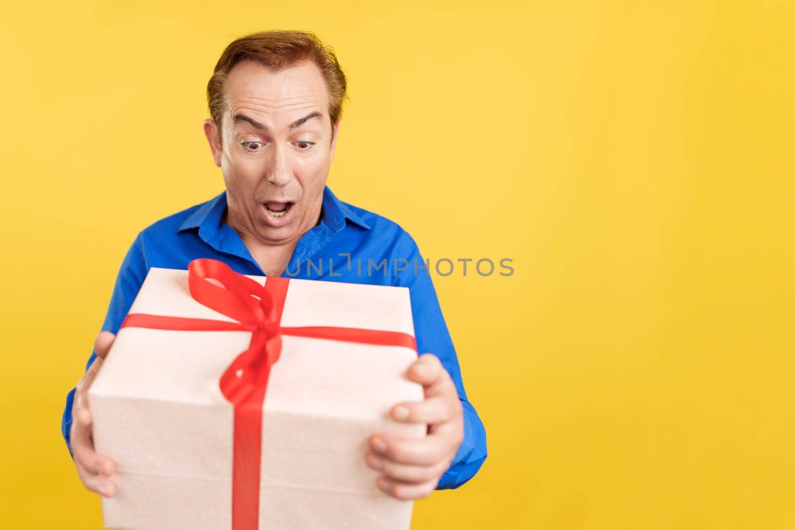 Happy mature man receiving a gift box in studio with yellow background