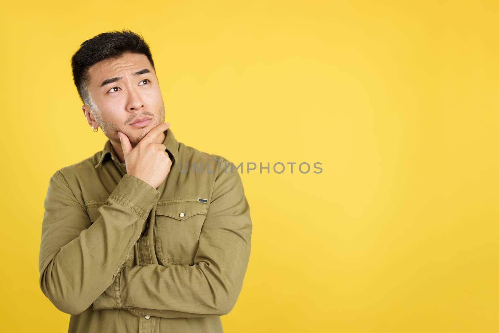 Chinese man with hand on face and thoughtful expression in studio with yellow background