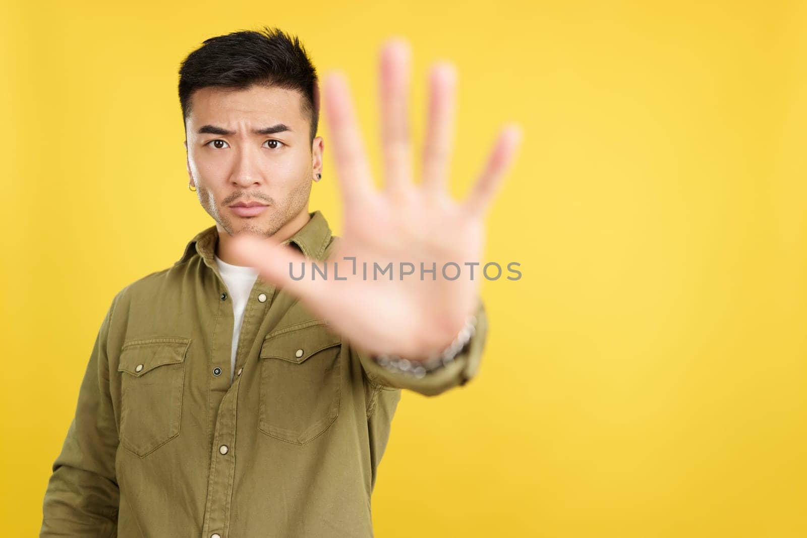 Chinese man gesturing prohibition with hand in studio with yellow background