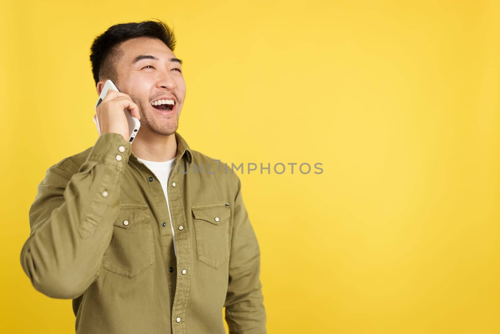 Happy chinese man talking to the mobile in studio with yellow background