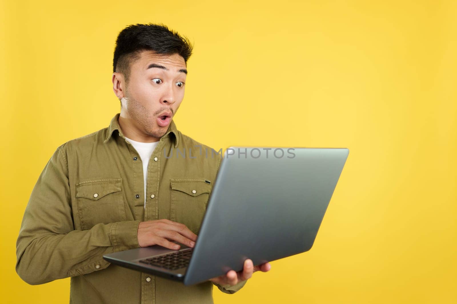 Chinese man with a surprised look using a laptop in studio with yellow background