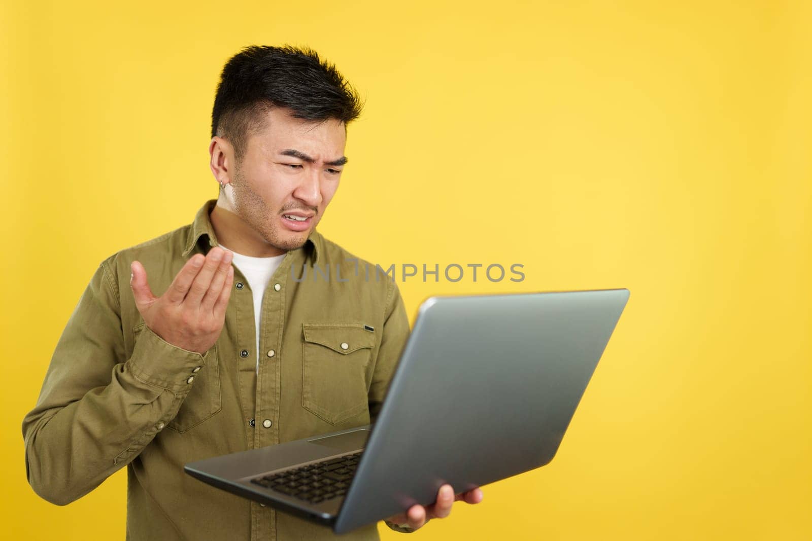 Chinese man having a problem with a laptop in studio with yellow background