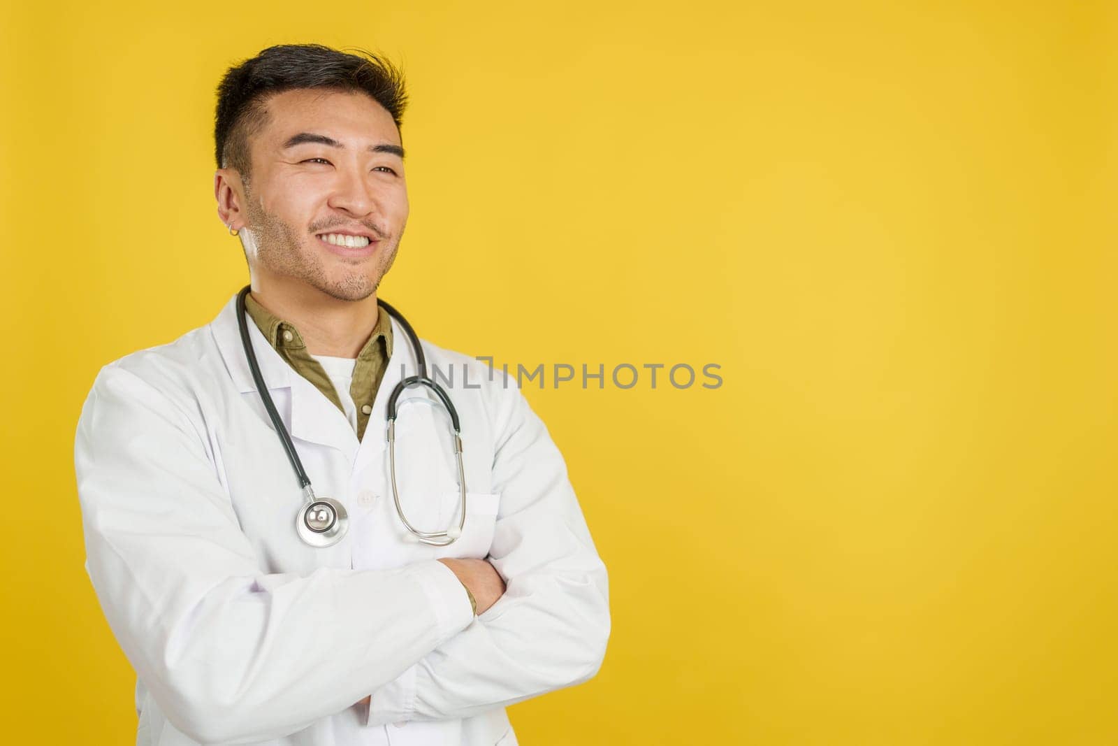 Friendly chinese doctor in uniform and stethoscope in studio with yellow background