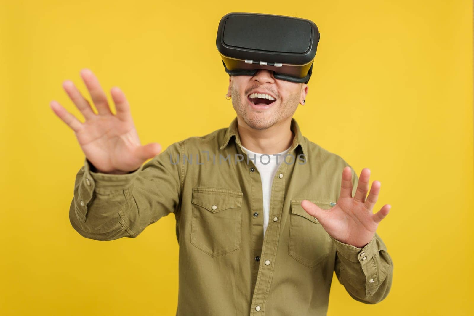 Happy chinese man with VR goggles expressing surprise in studio with yellow background