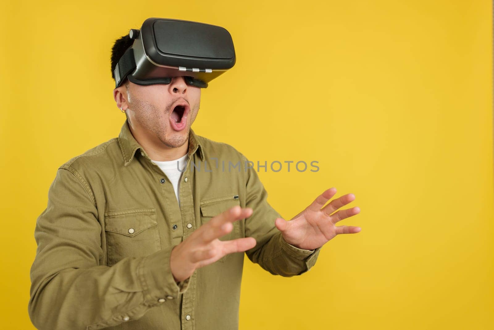 Chinese man with VR goggles expressing surprise in studio with yellow background
