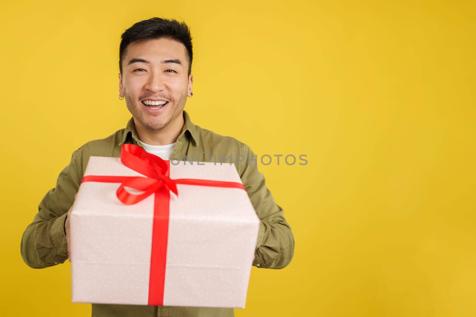 Happy chinese man looking at the camera giving a present in studio with yellow background