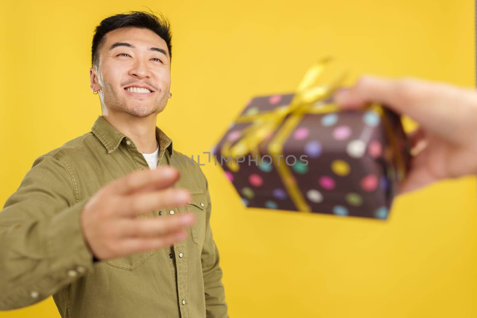 Happy chinese man smiling while receiving a gift in studio with yellow background