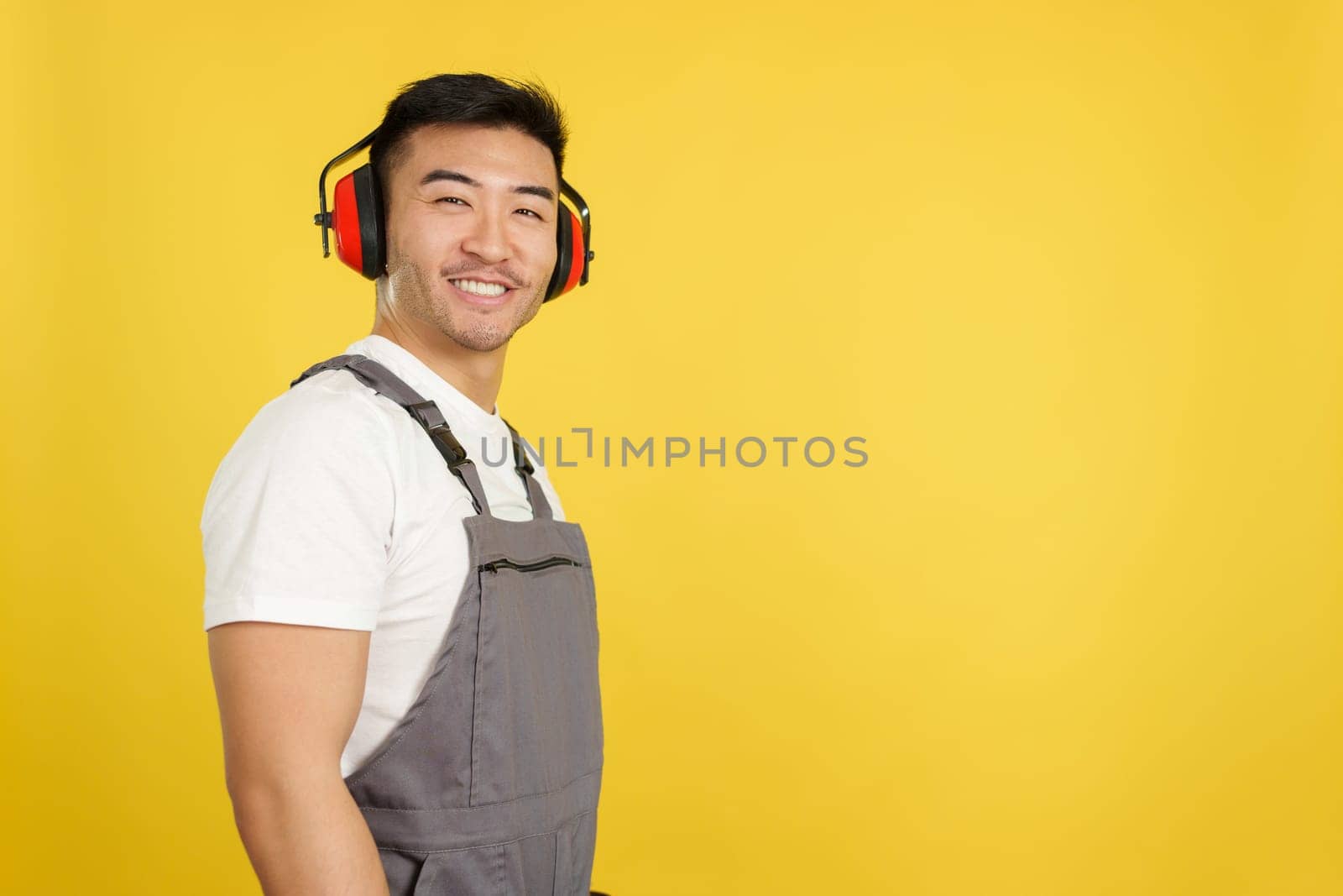 Chinese carpenter with protective gear smiling at the camera in studio with yellow background